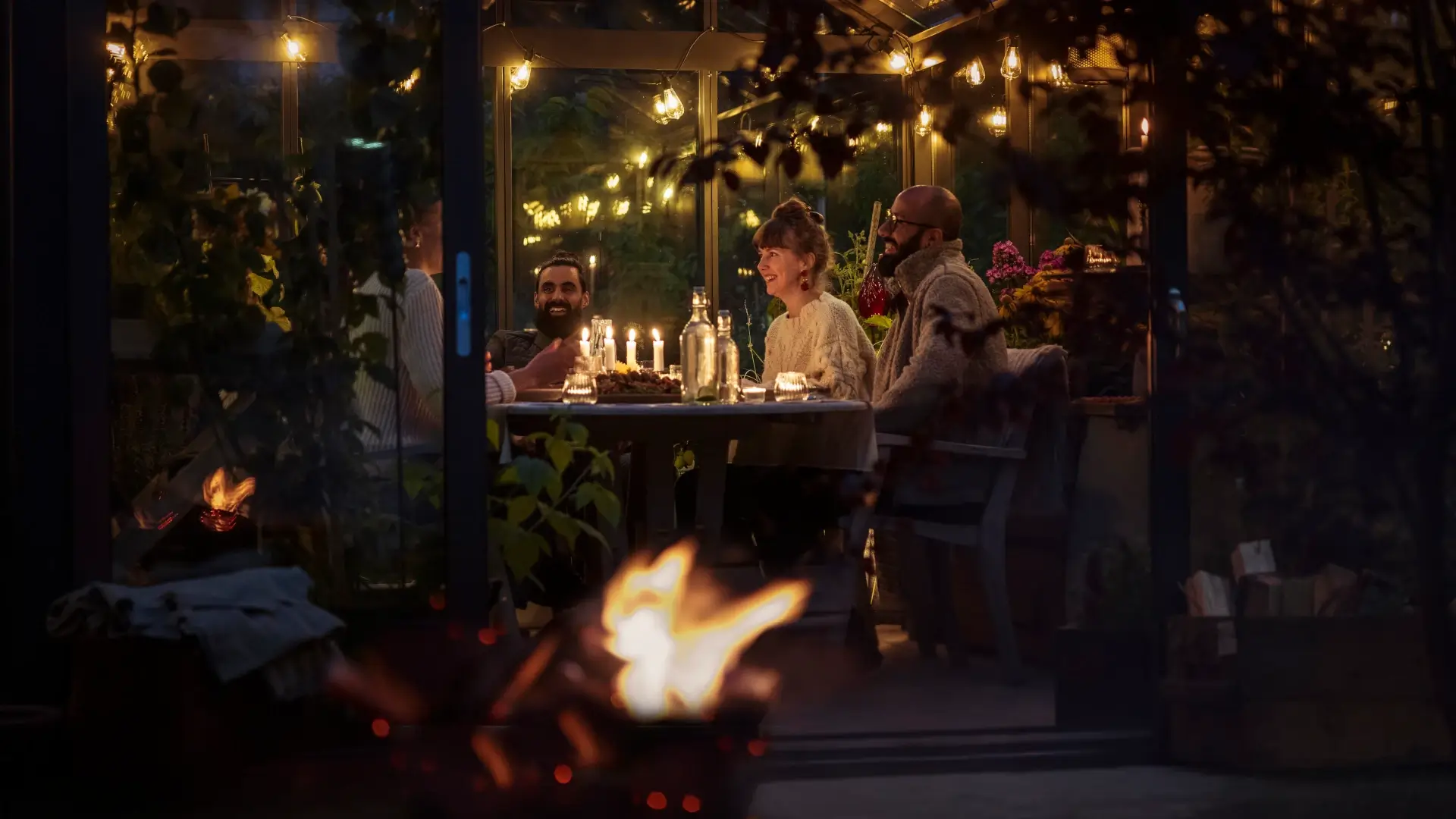 Group of friends sitting in a conservatory at night with a fire in the foreground